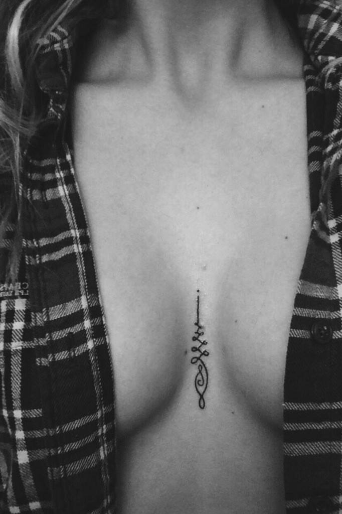 Unalome tattoo between breasts woman.