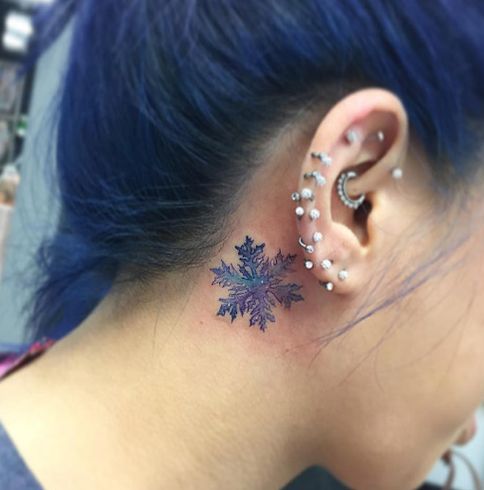 Blue and Purple Snowflake Tattoo behind the ear of a girl having pierced ear.